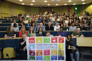 Business School staff in a lecture theatre holding the UN SDG flag