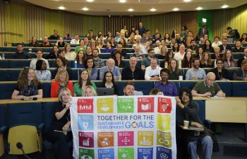 Business School staff in a lecture theatre holding the UN SDG flag