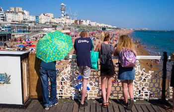 Four students stood looking away from the camera at Brighton beach, near the Palace Pier.