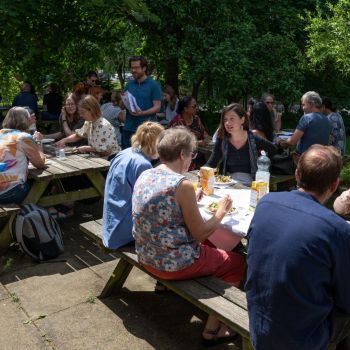 group of MAH faculty eat lunch together across picnic tables in Sussex Hums Lab garden