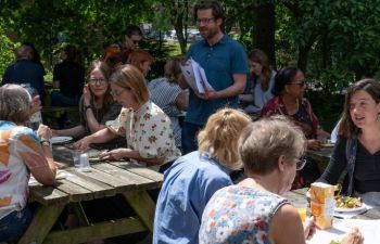 group of MAH faculty eat lunch together across picnic tables in Sussex Hums Lab garden