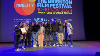 A photo showing the second prize winners of last years challenge! They are on a stage with the Brighton Film Festival Screen in the background.