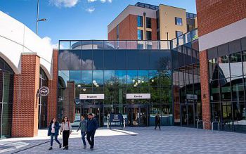 Four students outside of the University's Student Centre and one student walking into the Student Centre building.