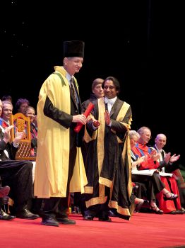 Geoffrey Hinton receives an honorary degree on stage, standing next to Chancellor Sanjeev Bhaskar OBE