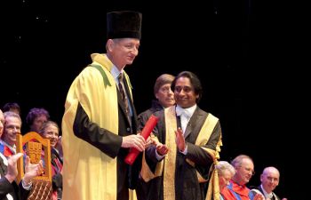 Geoffrey Hinton receives an honorary degree on stage, standing next to Chancellor Sanjeev Bhaskar OBE