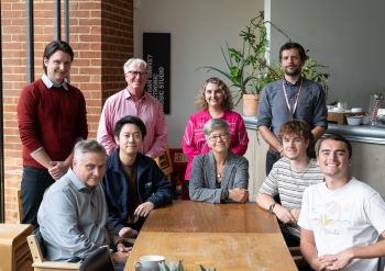 University of Sussex Vice-Chancellor Prof Sasha Roseneil sits in the centre of a group with students sat around a table, and staff standing behind her.