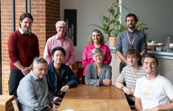 University of Sussex Vice-Chancellor Prof Sasha Roseneil sits in the centre of a group with students sat around a table, and staff standing behind her.