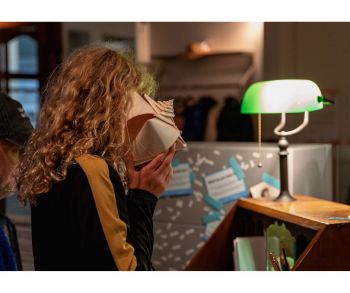 At the exhibition, a child holds a speaker shaped as a shell to their ear and listens in