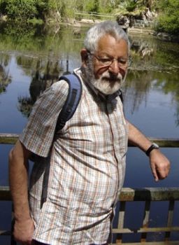 man with grey hair and beard standing by a pond