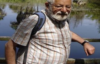 man with grey hair and beard standing by a pond