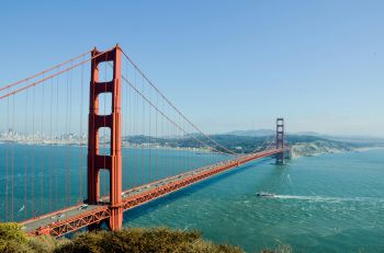 Image of Golden Gate Bridge, a tall red bridge in California, stretching over a bright blue sea and sky.