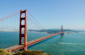 Image of Golden Gate Bridge, a tall red bridge in California, stretching over a bright blue sea and sky.