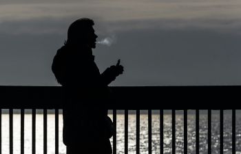 A backlit person smoking a vape beside the sea