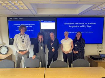 five people standing in front of large screens which display the presentation slides