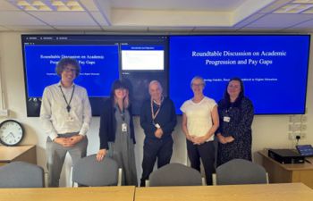 five people standing in front of large screens which display the presentation slides