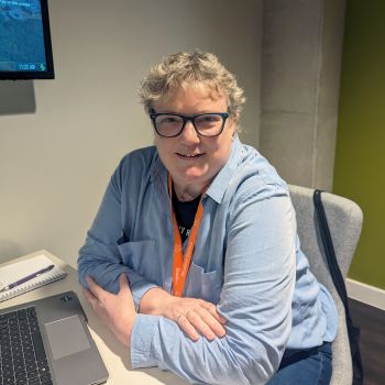 Mandy Healy leans on her desk and looks toward camera