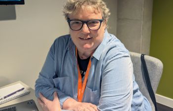 Mandy Healy leans on her desk and looks toward camera