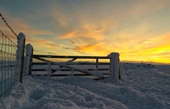 Winter sunrise across a snowy landscape with gate in foreground