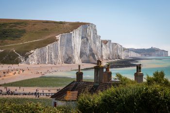 View of the white Sussex cliffs with fishermen's cottages in the foreground, and people walking on the beach