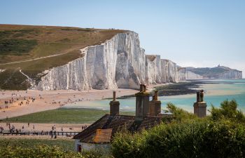 View of the white Sussex cliffs with fishermen's cottages in the foreground, and people walking on the beach