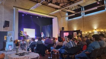 Audience watching a group of students seated on a stage and taking part in a workshop