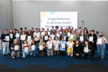 The 2024 cohort of Junior Research Associates smiling at the camera and holding their certificates of completion