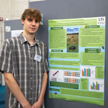 A student standing and smiling at the camera in front of their poster