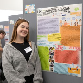 A student standing and smiling at the camera in front of their poster