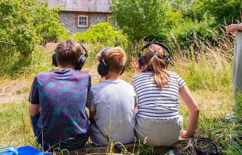 Children with headphones on looking at a grassy scene