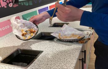 Diner's hands as they scrape food waste from their plate into the food waste bin, one of six recycling bins in Eat Central