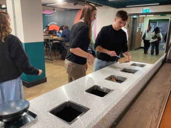 A woman helping a young male student to recycle food waste at the bins in Eat Central