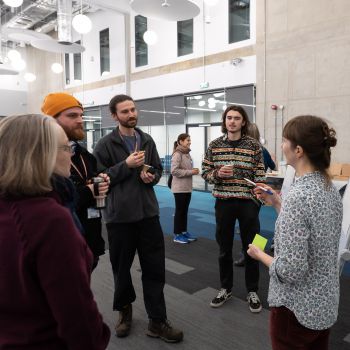 A group of workshop participants stand by a flipchart and listen to a member of staff talking at an event