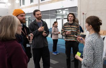 A group of workshop participants stand by a flipchart and listen to a member of staff talking at an event