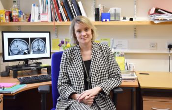 Dr Jessica Eccles from BSMS sat in an office with brain imagery on the computer behind her