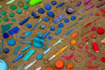 A rainbow of rubbish on the beach with items all laid out in the sand according to colour