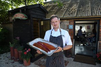 Mike King, a man, holding smoked fish outside a pretty British restaurant with trees and leaves visible