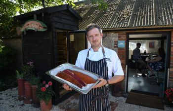 Mike King, a man, holding smoked fish outside a pretty British restaurant with trees and leaves visible