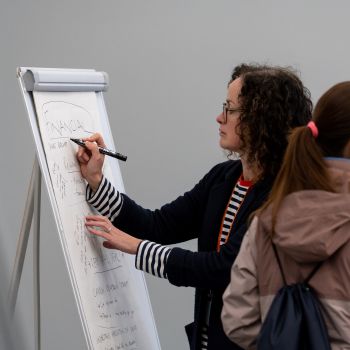 A member of staff writes on a flipchart, with some people around them at an event