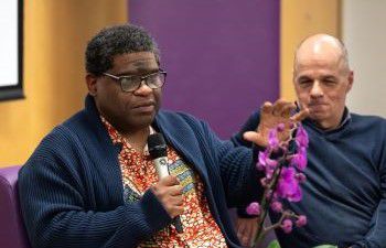 Gary Younge speaking with a microphone next to David Ruebain