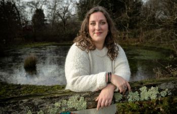 Canelle Tassin de Montaigu leans on an old fence in front of a pond in a clearing