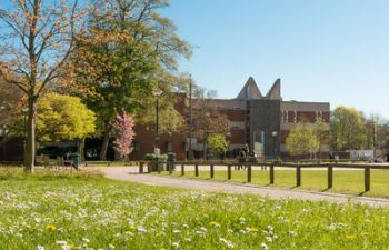 Photograph of grass, trees and Falmer House building on campus