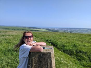 Zoe leans on a stone plinth in a green field