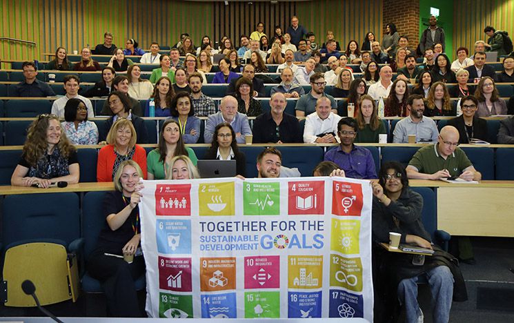 Business School staff holding the SDG (Sustainable Development Goals) flag in a small lecture theatre