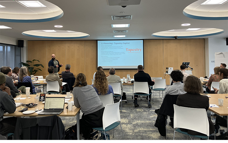 Research and community representatives at a collaborative workshop, sitting in a training room, watching a presentation on a screen