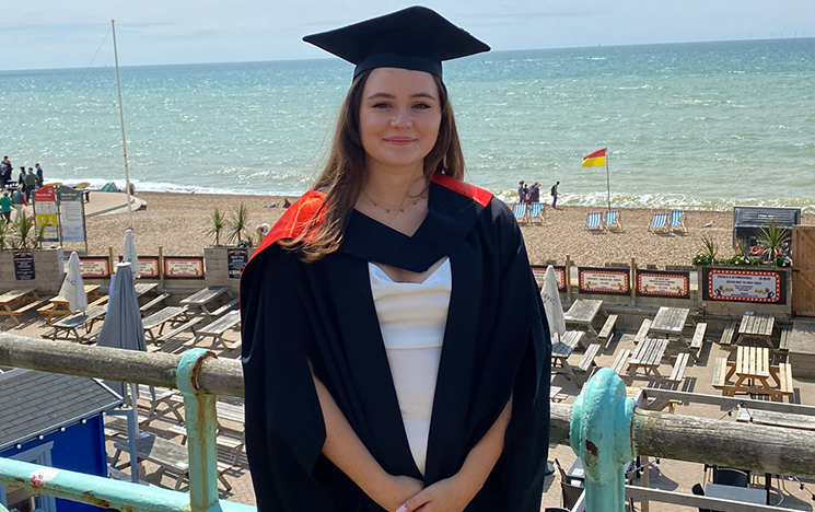 Emily Albon standing on Brighton seafront in a graduation gown.