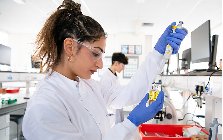 A student in a lab using a syringe to put liquid in a beaker.