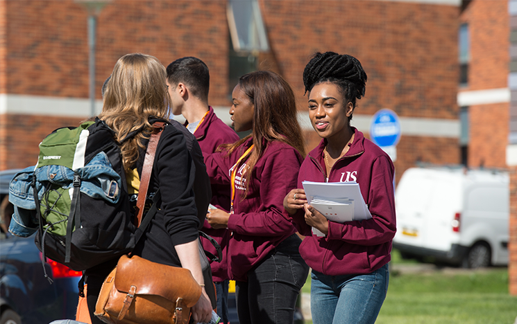 A student advisor holding paperwork who is talking to another student