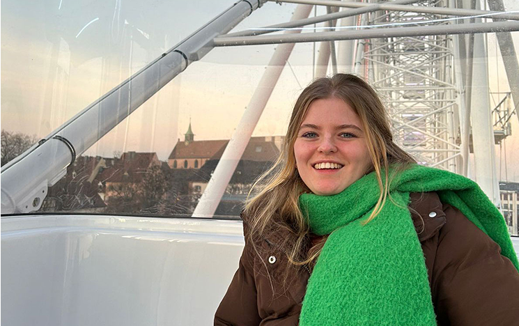 A woman sitting in a white ferris wheel carriage, wearing a green scarf and a brown coat