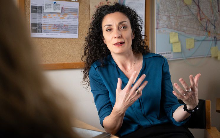 Dr Sarah Scuzzarello sitting at a table with another person, gesturing with her hands as she talks