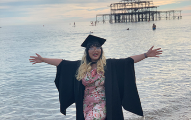 Huyen Le stood in her graduation gown on Brighton Beach with West Pier in the background.